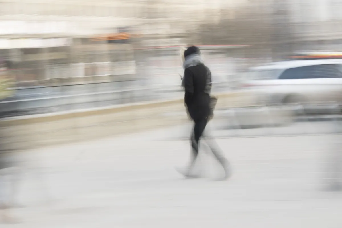 Hooded pedestrian crossing a wide street in soft motion blur